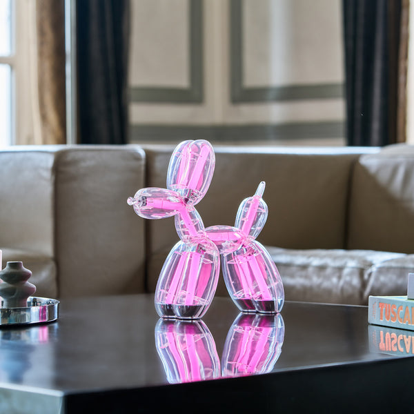 Eine rosa Glasballon-Hundeskulptur steht auf einem schwarzen Couchtisch in einem modernen Wohnzimmer.
