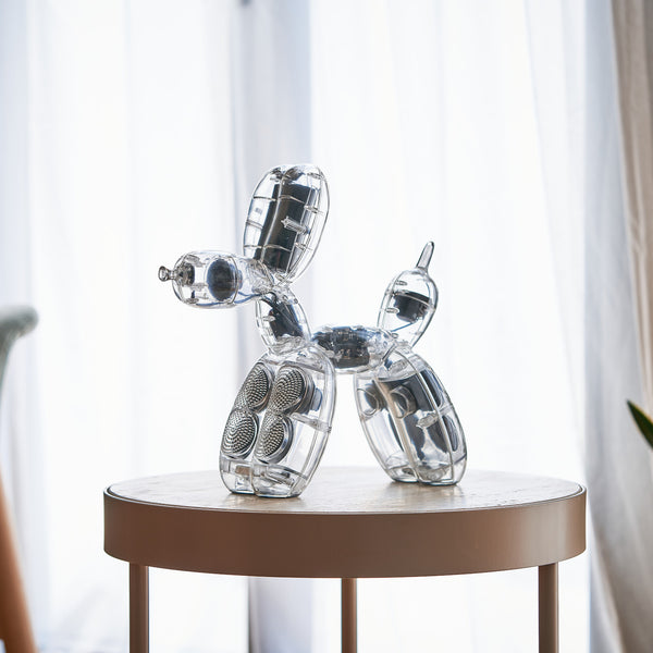 Eine transparente Ballonhundeskulptur steht auf einem runden beigen Tisch vor durchsichtigen Vorhängen.