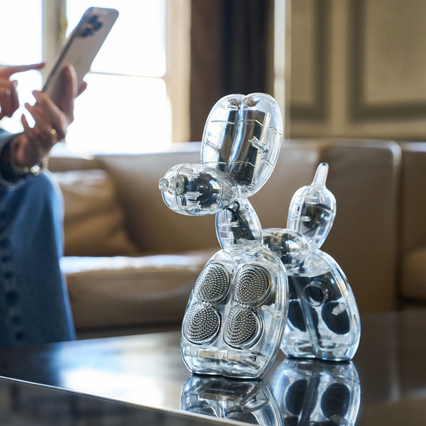 Eine Hundeskulptur aus einem durchsichtigen Plastikballon mit Lautsprechern im Inneren steht auf einem Tisch in der Nähe einer Person, die telefoniert.