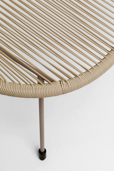 Nahaufnahme einer beigen Rattanoberfläche und dünnen Metallbeinen vor weißem Hintergrund.