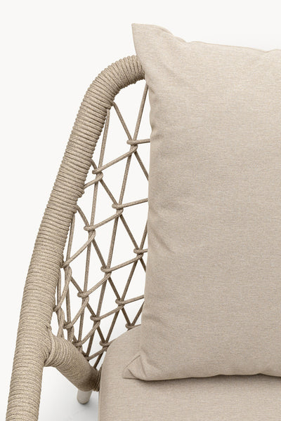 Nahaufnahme eines beigen Outdoor-Stuhls mit einem geflochtenen Seilrahmen und einem passenden Kissen vor einem schlichten Hintergrund.