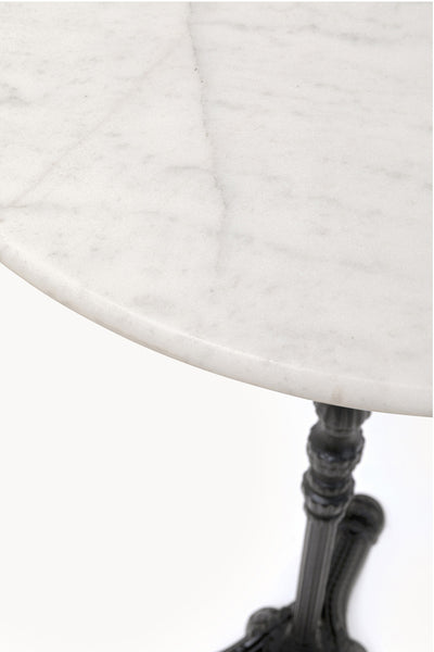 Runde Tischplatte aus weißem Marmor mit sichtbarer grauer Maserung, getragen von einem dunklen, verzierten Metallsockel, schräg von oben fotografiert.