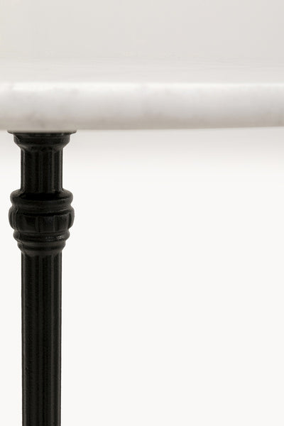 Nahaufnahme eines schwarzen, geriffelten Tischbeins, das eine glatte, weiße Marmortischplatte vor einem schlichten weißen Hintergrund trägt.