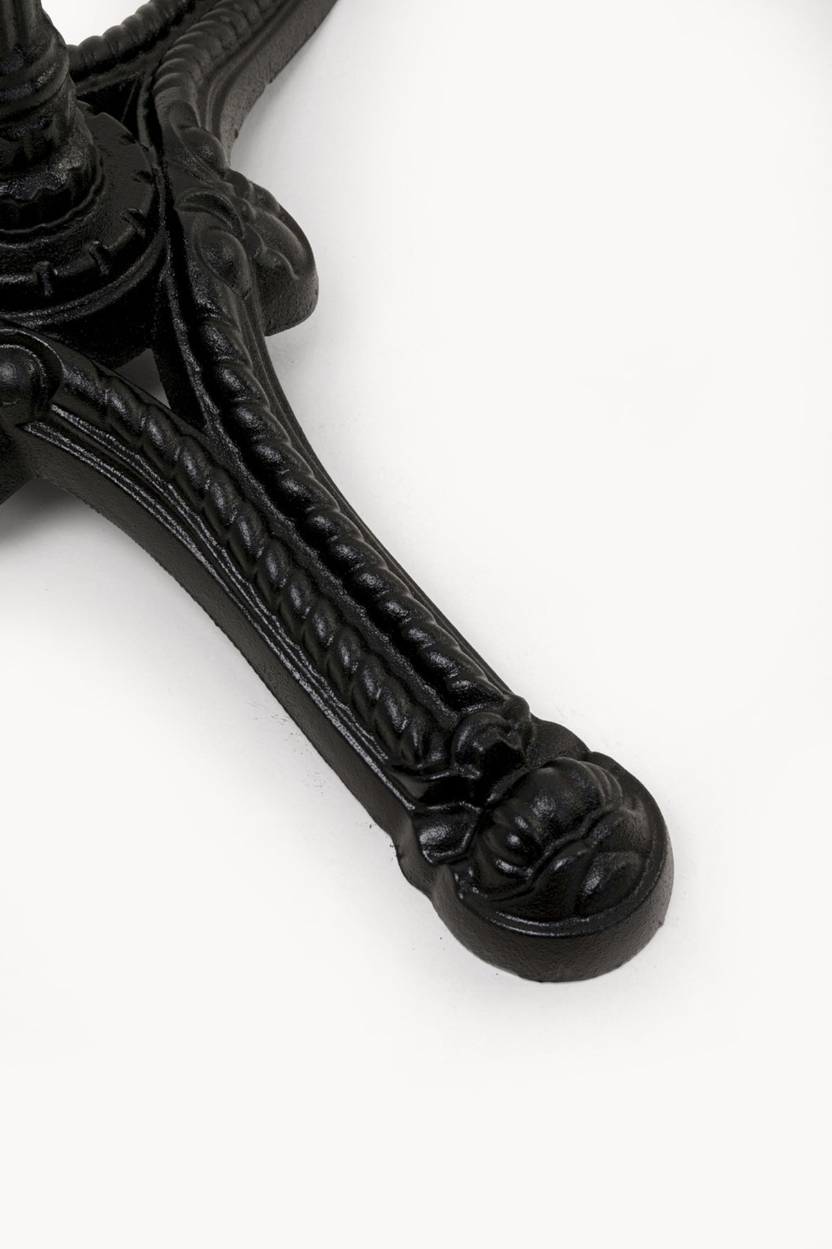 Nahaufnahme eines schwarzen, verschnörkelten Metalltischbeins mit dekorativen Details auf weißem Hintergrund.