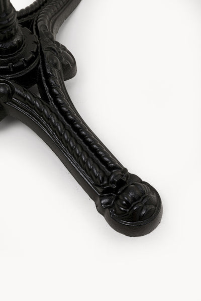 Nahaufnahme eines schwarzen, verschnörkelten Metalltischbeins mit dekorativen Details auf weißem Hintergrund.