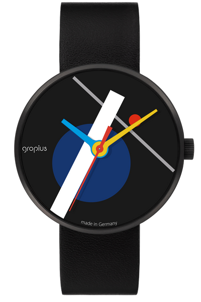 Eine moderne Armbanduhr mit schwarzem Lederband, minimalistischem Zifferblatt, geometrischen Formen, weißen und grauen Linien und blauen, gelben und roten Zeigern, mit der Aufschrift gropius made in Germany.