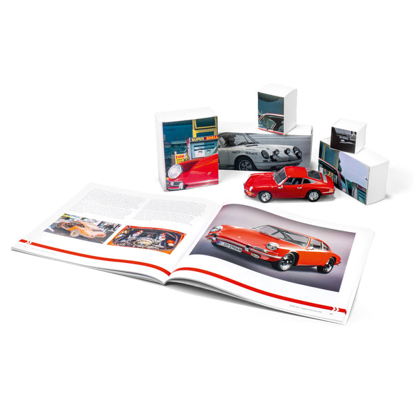 Ein aufgeschlagenes Autobuch neben einem roten Modellauto und kleinen Kästen mit Bildern von Oldtimern.
