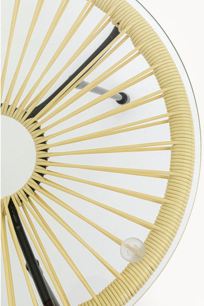 Draufsicht auf einen runden Glastisch mit beigefarbenem geflochtenem Rand und radialen Stützen; unter der Glasoberfläche sind ein Metallbein und ein kleines kugelförmiges Objekt zu sehen.