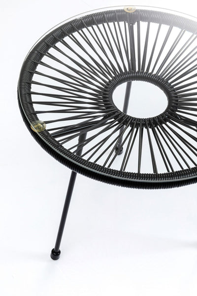 Runder Glastisch mit schwarzen Metallbeinen und einem kreisförmigen, geflochtenen schwarzen Rahmen, fotografiert vor einem weißen Hintergrund.