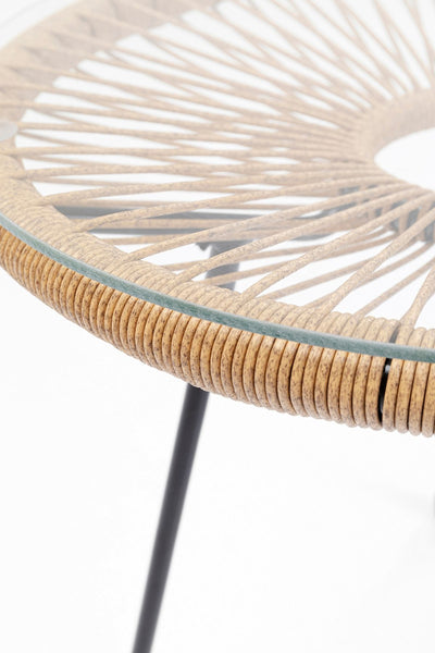 Nahaufnahme eines runden Glastischs mit geflochtener Rattankante und schwarzen Metallbeinen vor einem weißen Hintergrund.