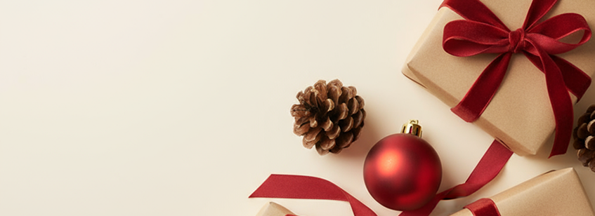 Geschenk mit rotem Schleifenband neben Tannenzapfen und roter Weihnachtsbaumkugel