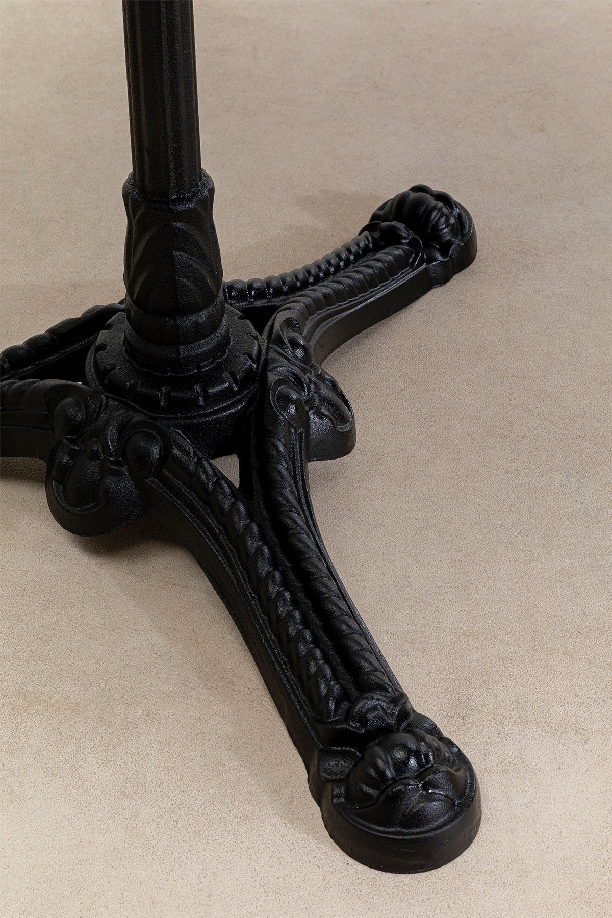 Schwarzer verschnörkelter Metalltisch mit drei Krallenfüßen, der auf einem beigen Teppichboden ruht.