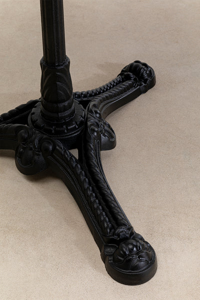 Schwarzer verschnörkelter Metalltisch mit drei Krallenfüßen, der auf einem beigen Teppichboden ruht.