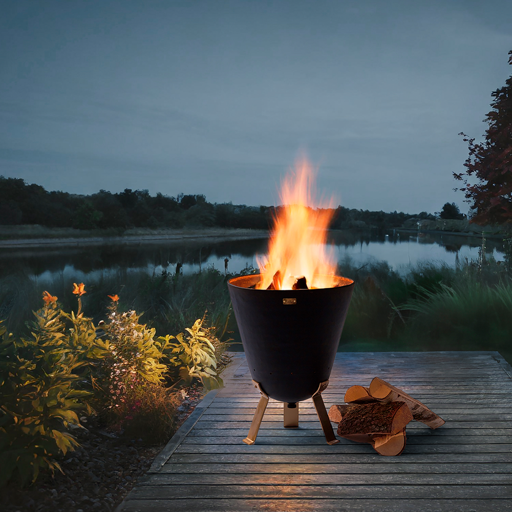 Brennende Feuerschale mit Brennholz nebendran am Steg eines Sees in einer schönen Naturlandschaft.