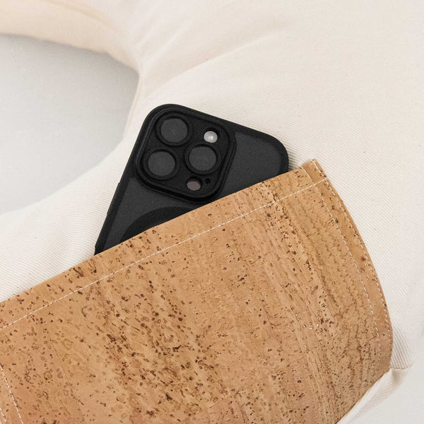 Ein Smartphone mit schwarzem Gehäuse, das teilweise in eine hellbraune Tasche mit Korkstruktur auf einer cremefarbenen Oberfläche gesteckt wurde.