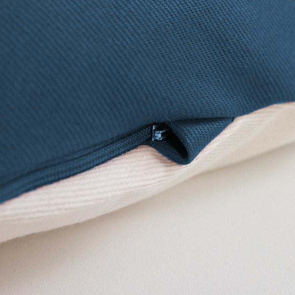 Nahaufnahme eines blauen Reißverschlusses an einem Kissen mit dunkelblauem Stoff auf der Oberseite und beigem Stoff auf der Unterseite.