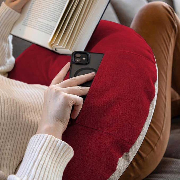 Eine Person, die ein Buch liest und das Telefon in der Tasche eines roten Kissens auf dem Schoß hat.
