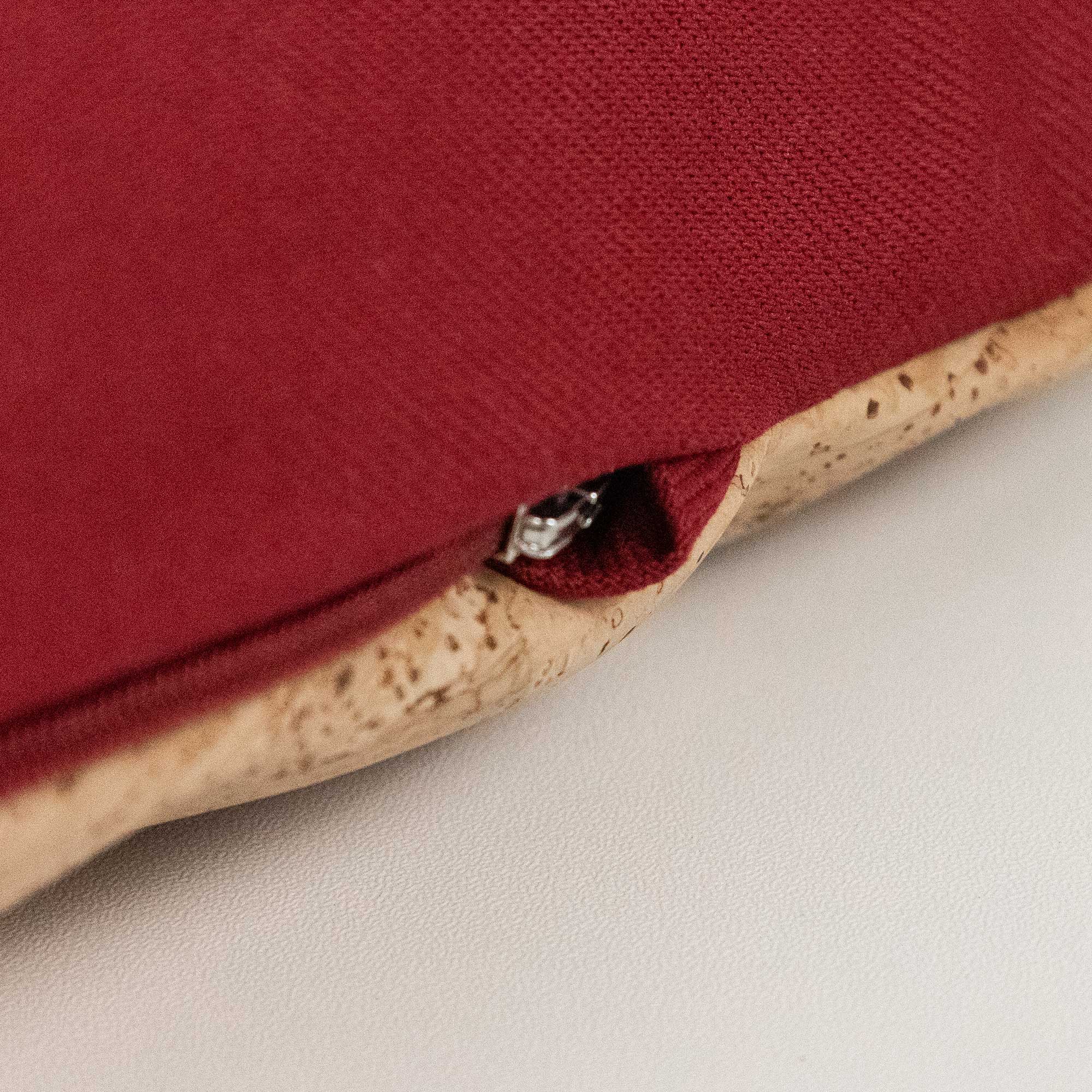 Nahaufnahme eines roten Stoffkissens mit sichtbarem Reißverschluss und korkartigem Rand auf einer weißen Fläche.