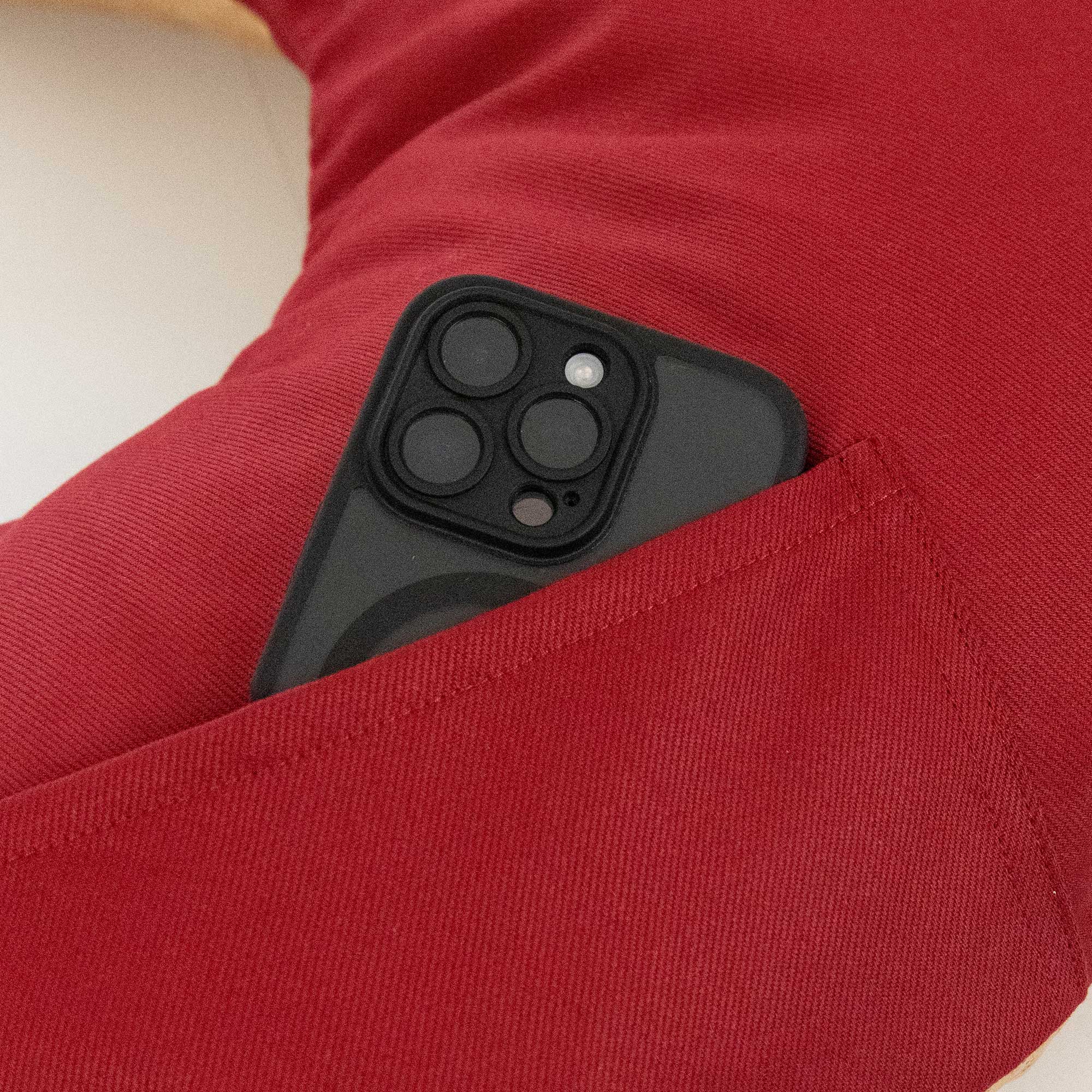 Ein schwarzes Smartphone, das teilweise in eine Tasche auf einer roten Stoffoberfläche gesteckt ist.