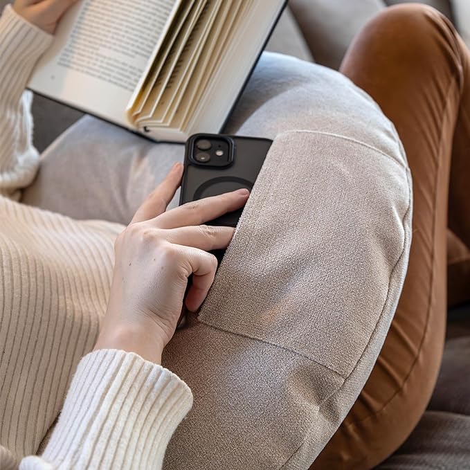 Mit dem Lesekissen Classic mit Tasche - Creme sitzt man im Schneidersitz und genießt ein Buch in optimalem Komfort, während das Smartphone teilweise in der Hosentasche steckt.