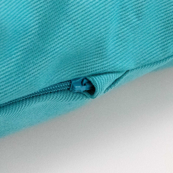 Nahaufnahme eines türkisfarbenen Stoffes mit einem passenden, teilweise geöffneten Reißverschluss, der auf einer weißen Fläche liegt.