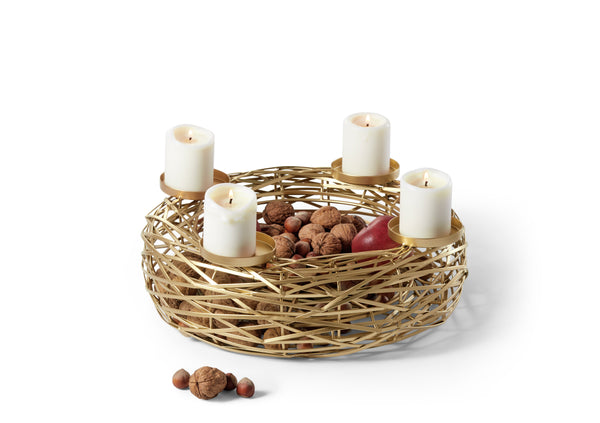 In einem goldenen Korb befinden sich vier brennende Kerzen, Nüsse und ein Apfel, wobei zusätzliche Nüsse außerhalb des Korbes verstreut sind.