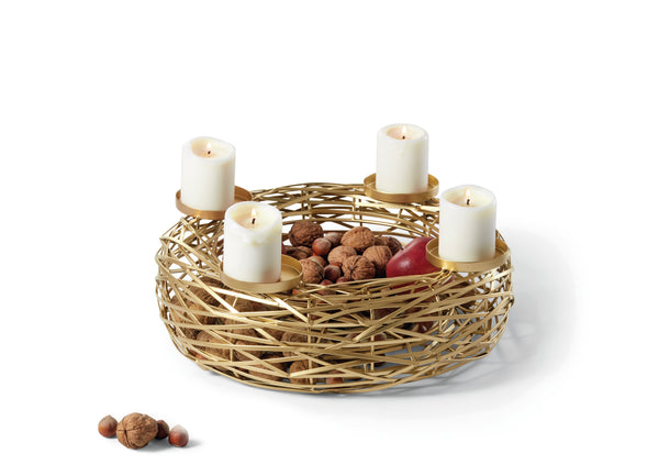 Golddrahtkorb mit vier brennenden Kerzen, Nüssen und einem Apfel darin; weitere Nüsse in der Nähe verstreut.