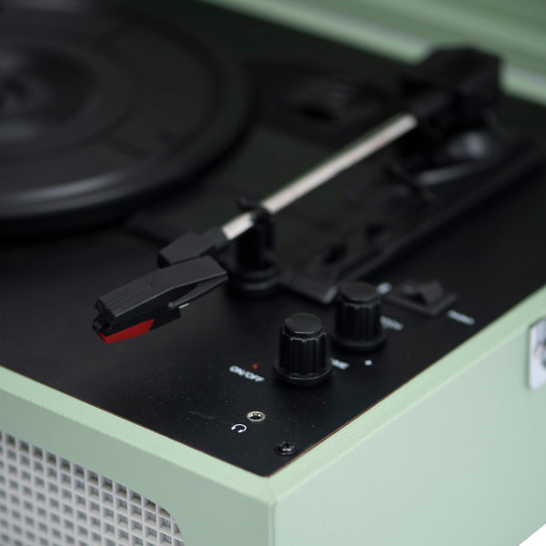 Nahaufnahme eines alten Plattenspielers mit Bedienelementen und einem Tonarm auf einer grünen Fläche.