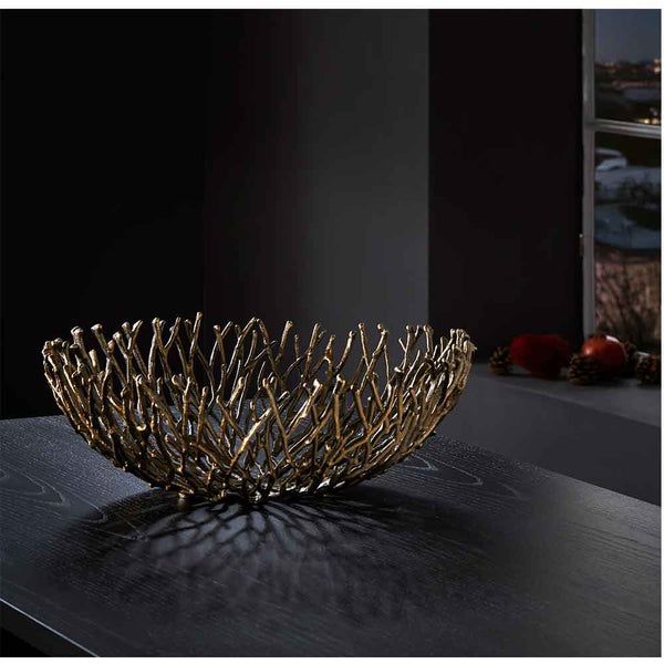 Eine dekorative Metallschale mit einem astähnlichen Muster steht auf einem dunklen Holztisch in einem schwach beleuchteten Raum.