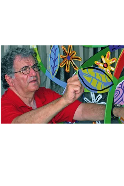 Ein älterer Mann mit Brille und rotem Hemd malt bunte Blätter und Blumen auf ein großes dekoratives Kunstwerk. David Gerstein der Künstler 