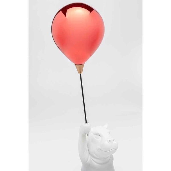 Eine weiße Nilpferdfigur hält einen Stock mit einem glänzenden roten Luftballon auf der Spitze vor einem schlichten Hintergrund.