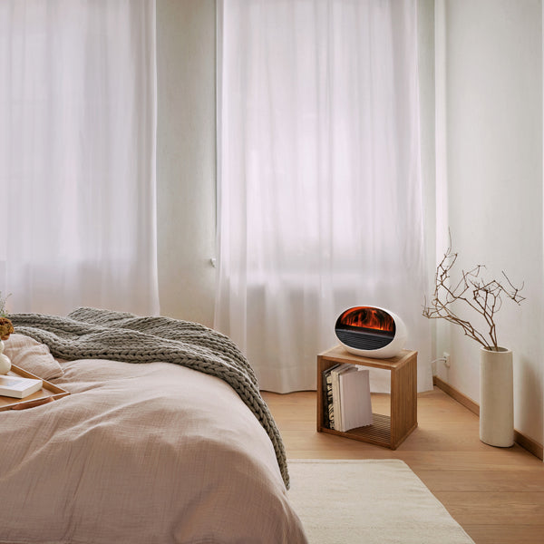 Gemütliches Schlafzimmer mit weicher Bettwäsche, durchsichtigen Vorhängen, einem hölzernen Beistelltisch und einem kleinen elektrischen Kaminheizgerät.