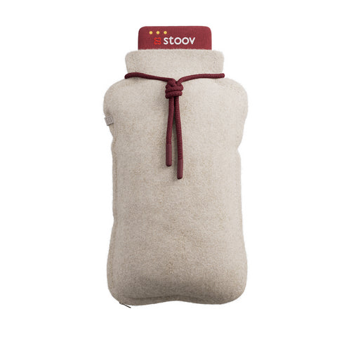 Eine beigefarbene Wärmflasche mit Fleeceüberzug und einer roten Kappe mit der Aufschrift stoov und einer roten Kordel, die um den Deckel gebunden ist.