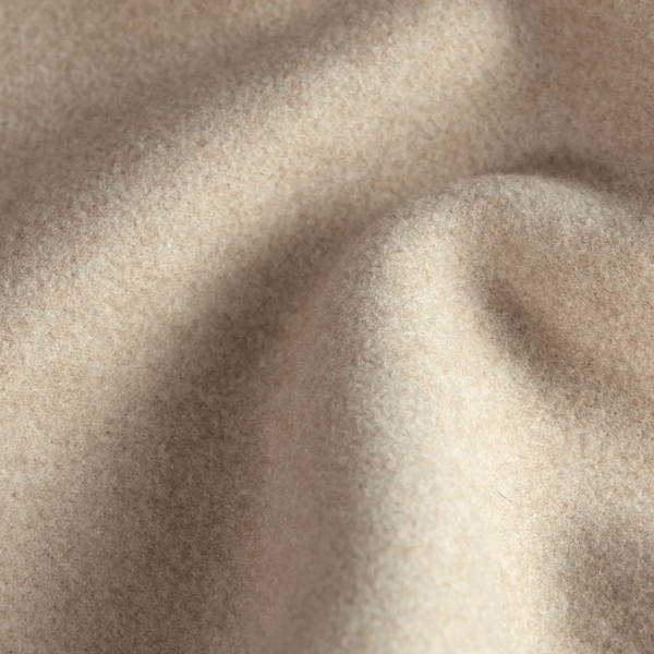 Nahaufnahme eines weichen, beigen Wollstoffs mit sanften Falten und einer glatten, flauschigen Textur.