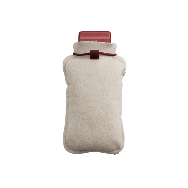Eine beigefarbene Wärmflasche mit einem weichen Stoffüberzug und einer roten Kappe, von oben gesehen auf weißem Hintergrund.