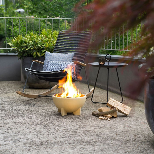 Eine gemütliche Terrasse mit einem Schaukelstuhl, einem kleinen Tisch, einer Feuerstelle und Brennholz auf einem Betonboden.