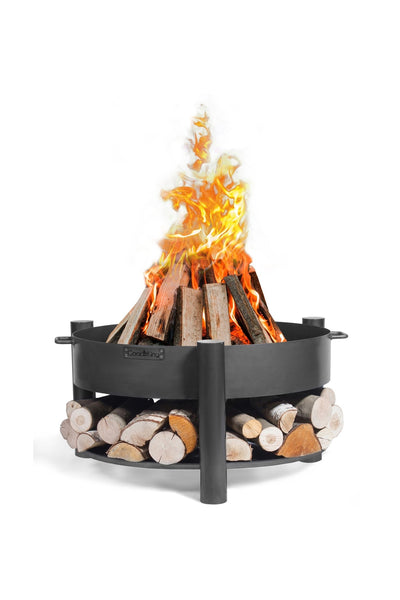 Eine Feuerstelle aus Metall mit einem brennenden Holzfeuer, mit einer unteren Ablage für zusätzliches Brennholz, vor einem weißen Hintergrund.