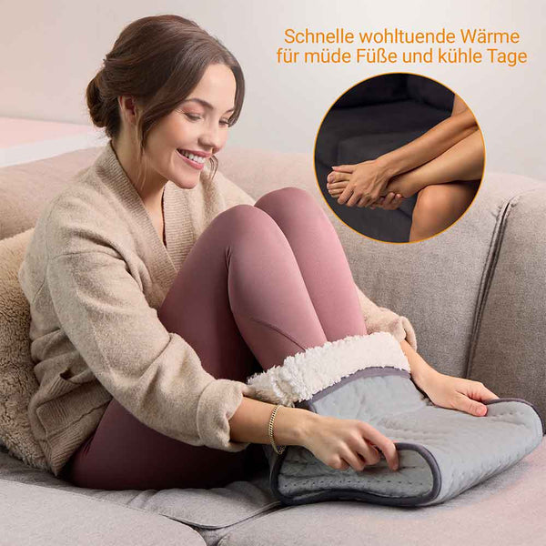 Frau sitzt auf einer Couch und wärmt ihre Füße in einem beheizten Fußwärmer; deutscher Text wirbt für dessen Komfort.