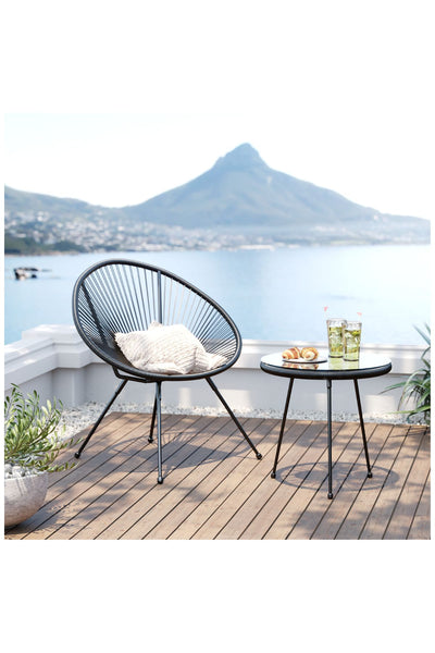 Ein moderner schwarzer Stuhl und ein runder Tisch mit Getränken und Gebäck auf einer Terrasse mit Blick auf ein ruhiges Gewässer und einen fernen Berg.