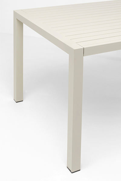Eine Nahaufnahme der Ecke eines rechteckigen, hellbeigen Tisches mit einer Lattenplatte und geraden, quadratischen Beinen.