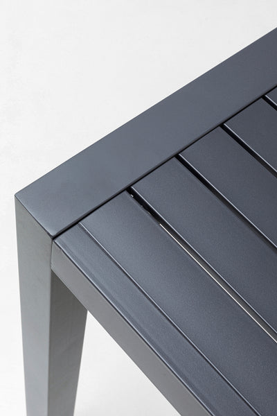 Nahaufnahme eines grauen Metalltisches mit einer Lattenplatte und quadratischen Beinen, fotografiert vor einem schlichten weißen Hintergrund.