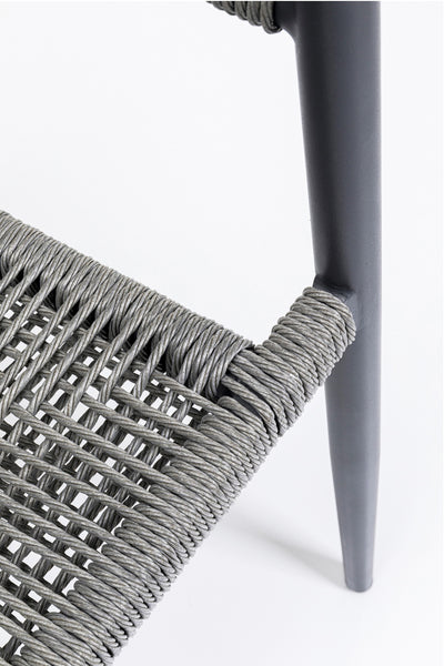 Nahaufnahme eines Stuhls mit geflochtener Sitzfläche und Rückenlehne aus grauem Cord, mit dunkelgrauen Metallbeinen.