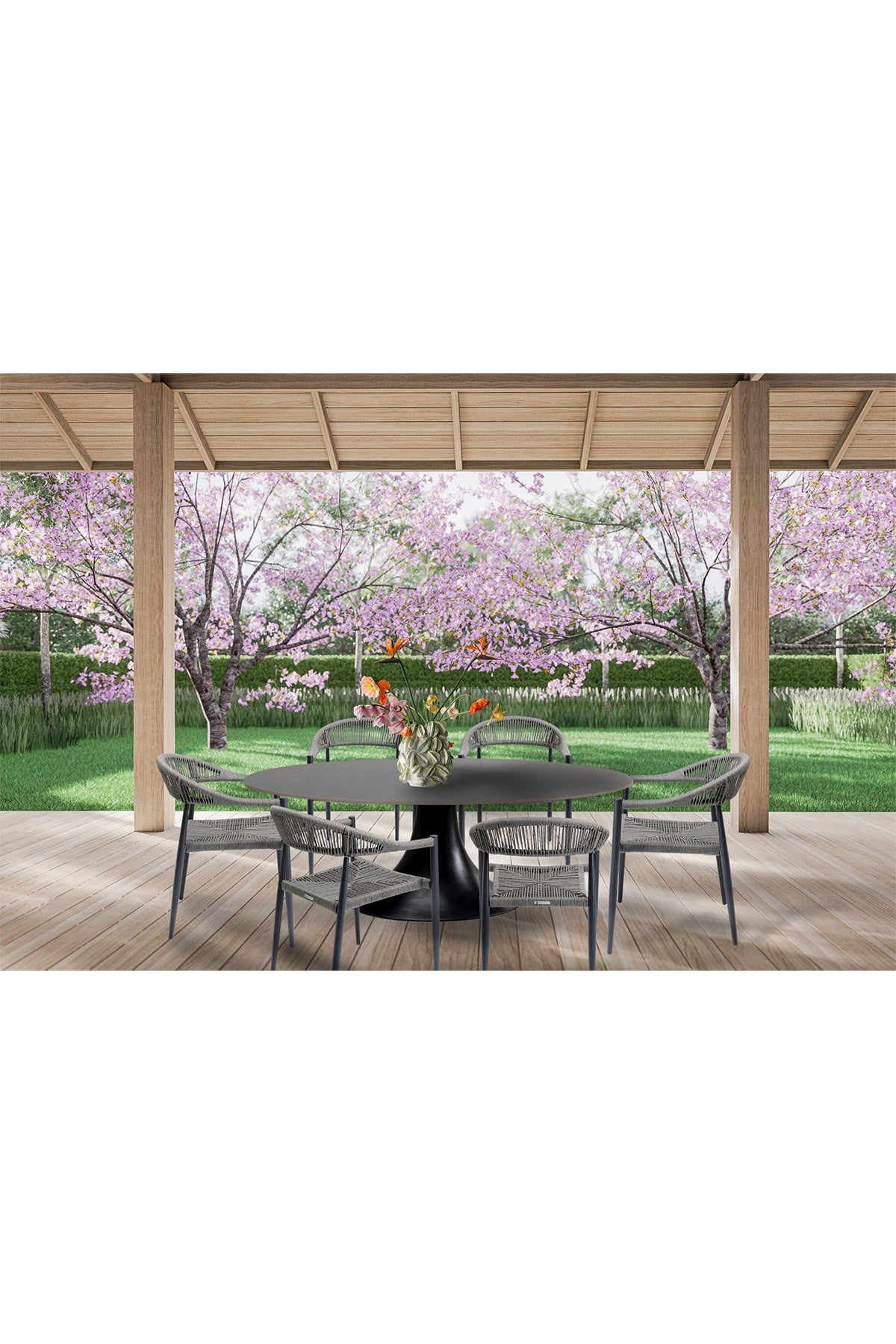 Terrasse mit rundem Tisch, sechs Stühlen und einer Blumenvase mit Blick auf einen Garten mit rosa blühenden Bäumen und grünem Gras.