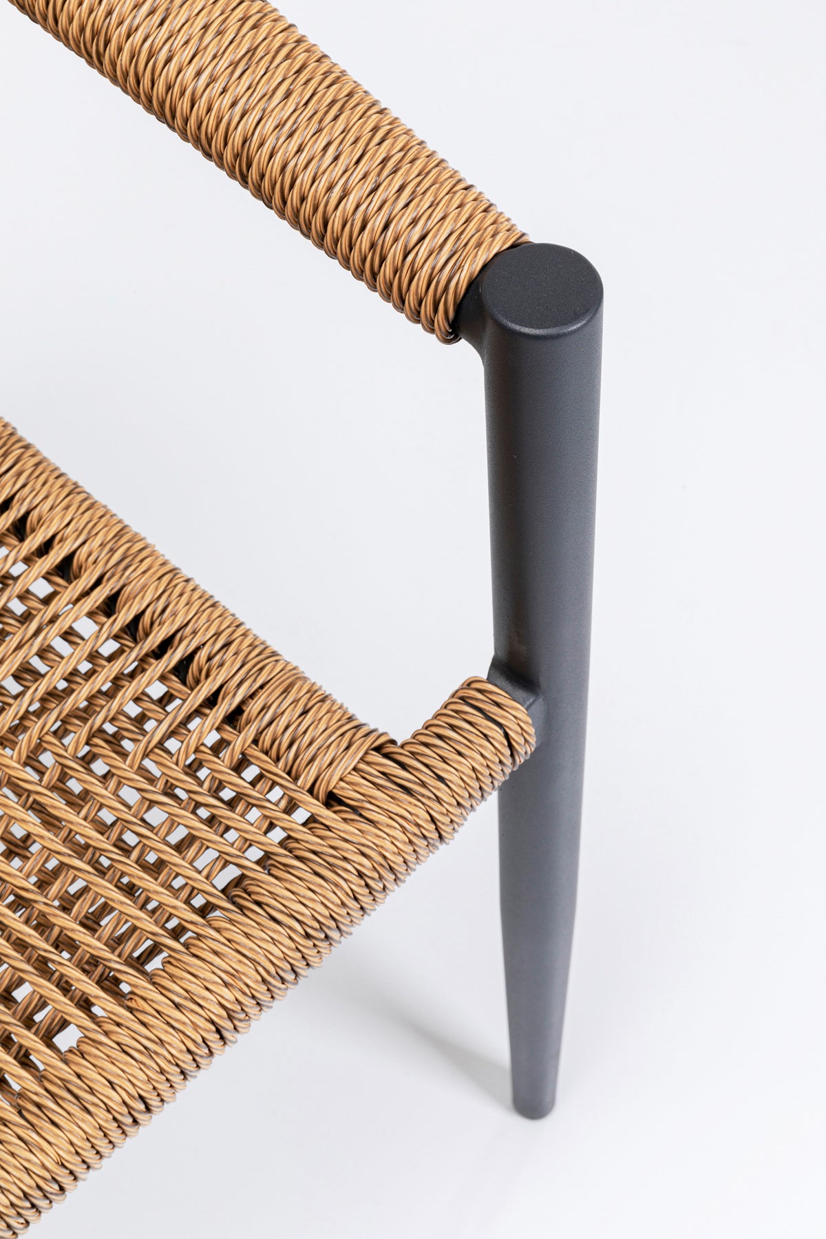 Nahaufnahme einer Stuhlecke mit Sitz und Rückenlehne aus geflochtener Naturfaser und einem eleganten, mattschwarzen Metallrahmen vor weißem Hintergrund.