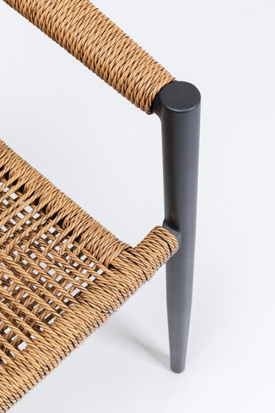 Nahaufnahme einer Stuhlecke mit Sitz und Rückenlehne aus geflochtener Naturfaser und einem eleganten, mattschwarzen Metallrahmen vor weißem Hintergrund.