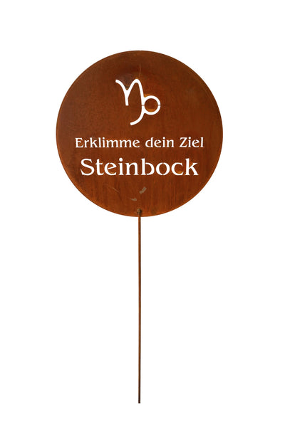 Rundes Metallschild mit dem Steinbock-Symbol, dem deutschen Text Erklimme dein Ziel Steinbock und einem dünnen Metallpflock am unteren Ende.