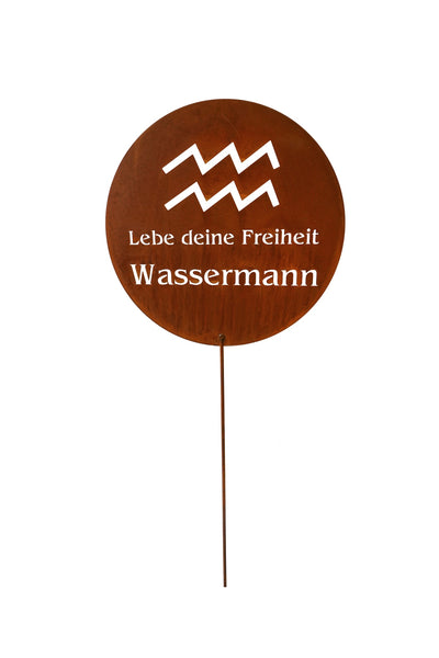 Ein rundes braunes Schild mit dem Tierkreiszeichen des Wassermanns und dem deutschen Text Lebe deine Freiheit Wassermann, montiert auf einem dünnen Metallstab.