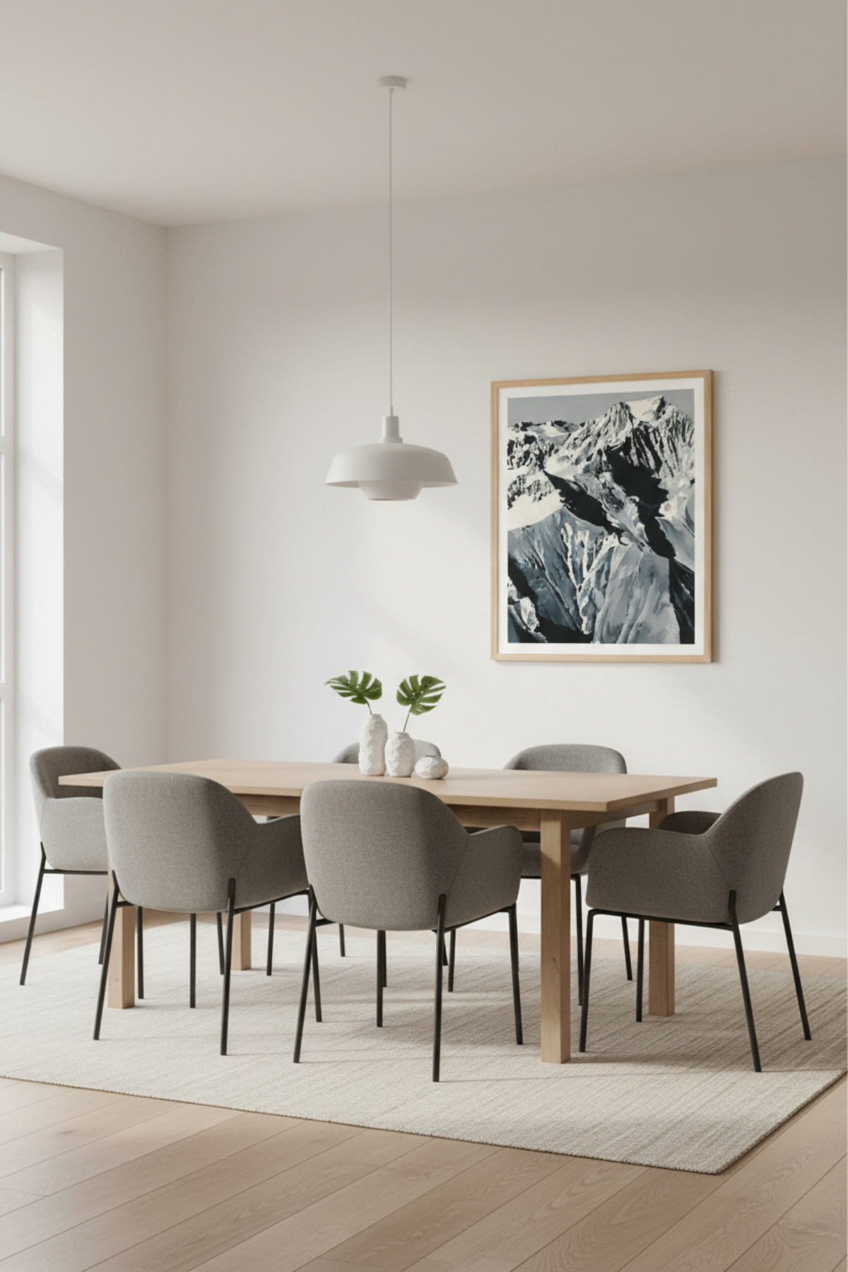 Minimalistisches Esszimmer mit einem Holztisch, sechs grauen Stühlen, einer weißen Pendellampe, einem hellen Teppich und einem gerahmten Bergfoto an der Wand.