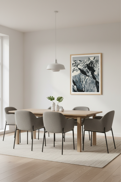 Minimalistisches Esszimmer mit einem Holztisch, sechs grauen Stühlen, einer weißen Pendellampe, einem hellen Teppich und einem gerahmten Bergfoto an der Wand.