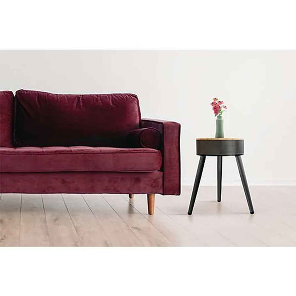 Ein weinrotes Sofa neben einem kleinen schwarzen Beistelltisch mit einer Vase mit rosa Blumen darauf.